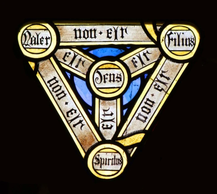 Fig 6: Left: Sabian Symbol #5: The white triangle with golden wings ( by: Cosmic Program). Right: The Holy Trinity on the stained glass windows of the Church of SS Peter and Paul in Brockdish. Source: Unknown, CC BY-SA 2.0 < https://creativecommons.org/licenses/by-sa/2.0 >, via Wikimedia Commons